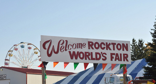 Sign welcoming visitors to the Rockton World's Fair. Ferris Wheel, barns, and marquees in background